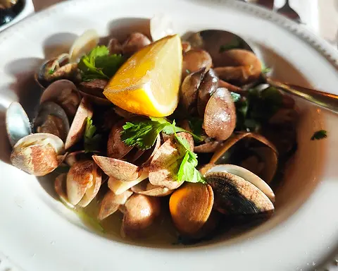 A bowl of clams in broth with coriander and a lemon wedge