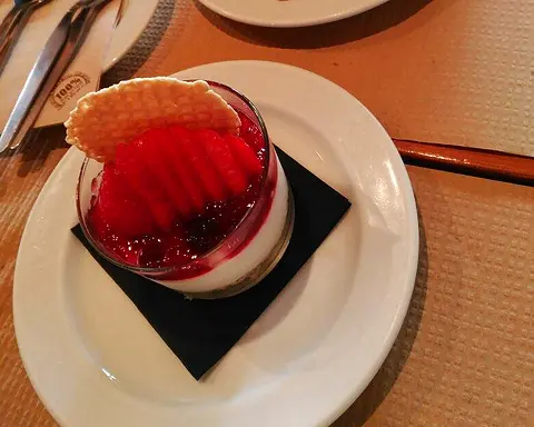 A creamy dessert in a glass topped with red fruit and a wafer