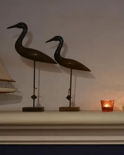 Two carved wooden wading birds and a lit candle on the dining-room mantelpiece